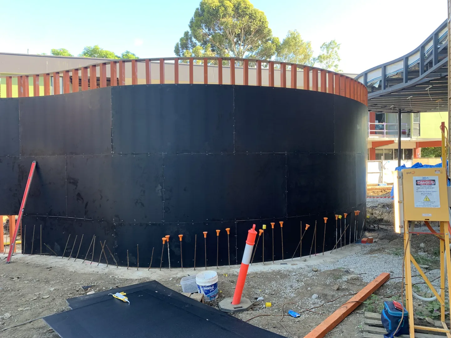 Curved building under construction with black exterior panels.