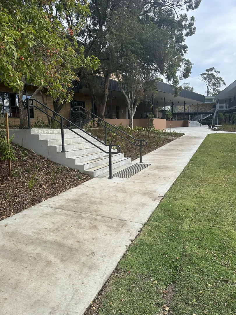 Concrete pathway next to building with steps and railings.