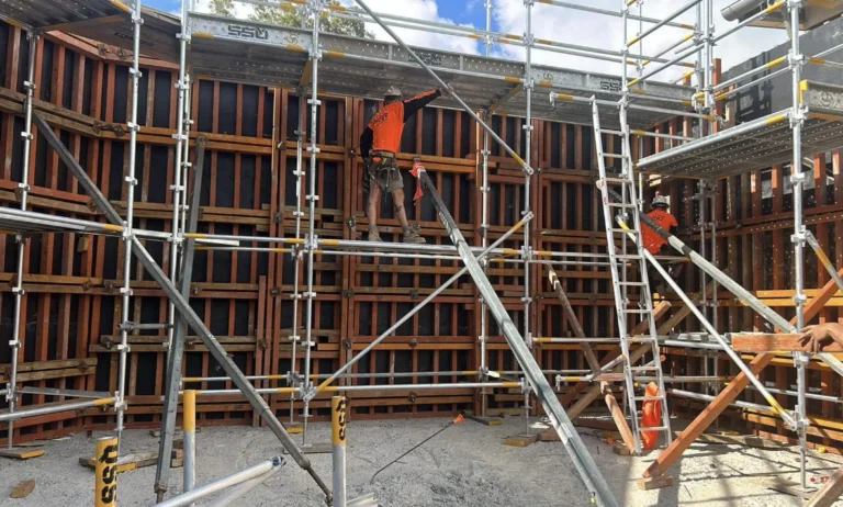 Construction workers on scaffolding building a wooden wall.